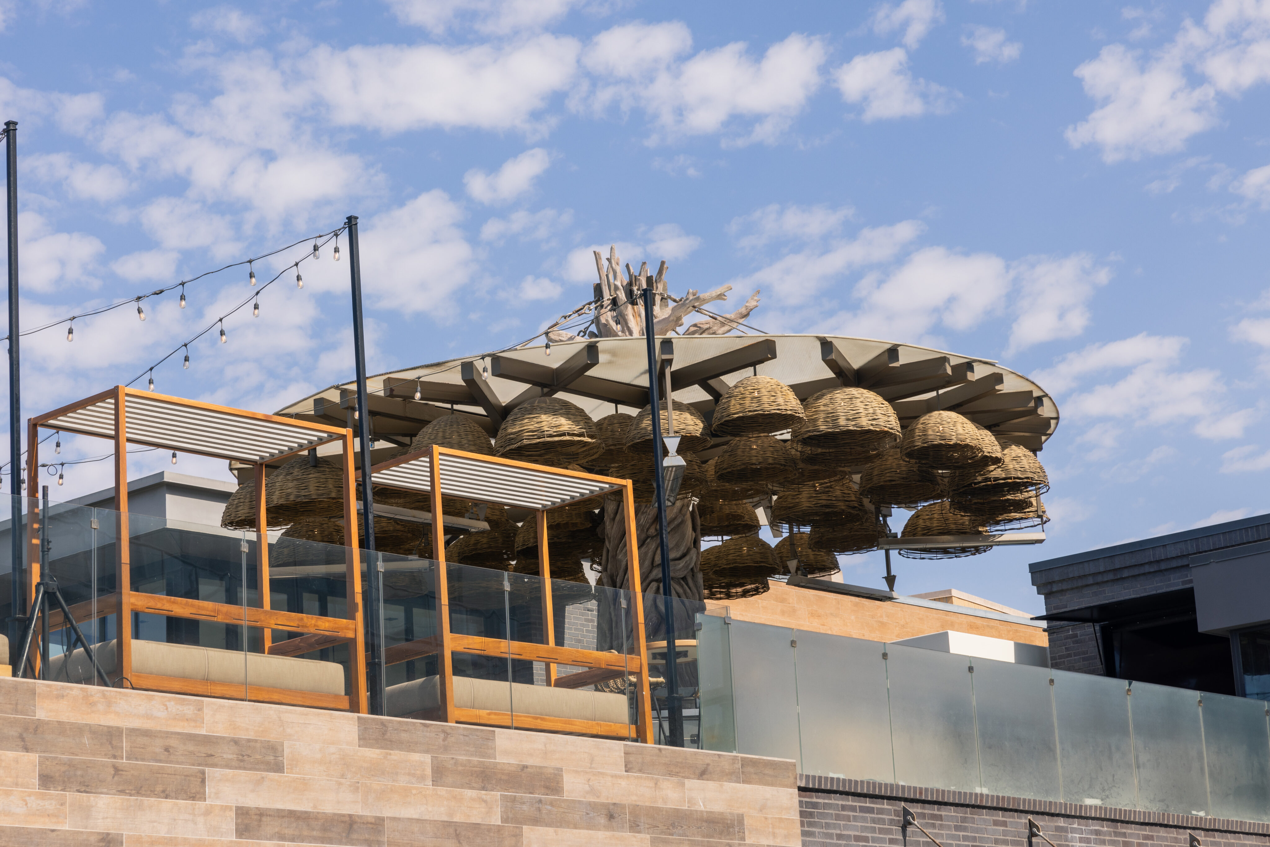 Outdoor rooftop area with wooden pergolas and a structure featuring multiple large woven basket-like decorations under a partly cloudy sky.