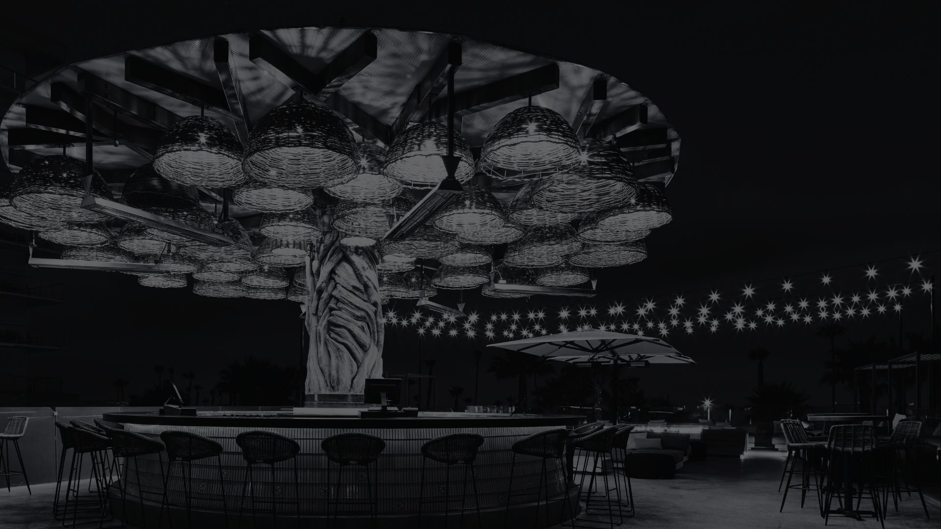 A modern outdoor bar with woven basket-style lights creates an Enchanted Treehouse canopy over the counter, with string lights and seating glowing in the background at night.